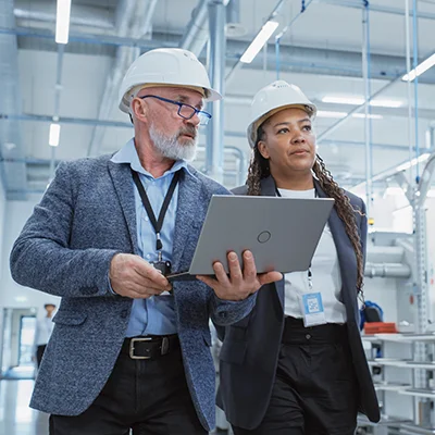 two business people wearing hard hats inspecting an manufacturing facility