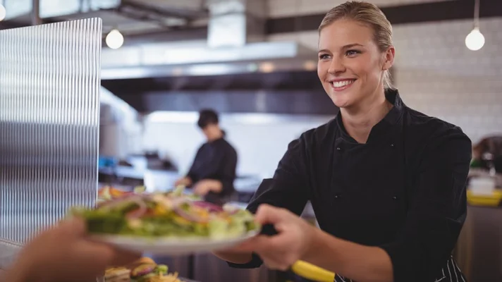 commercial kitchen worker handing a plate to a waiter