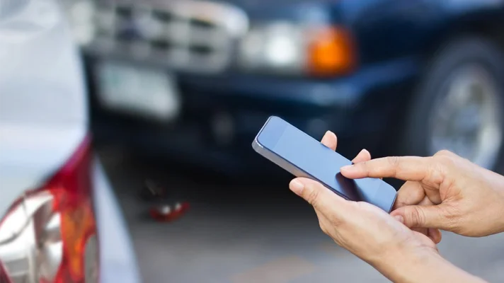 close up of hands texting on a phone with an auto accident in the background