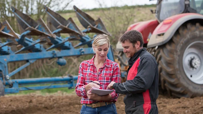 two people conversing in front of farm equipment