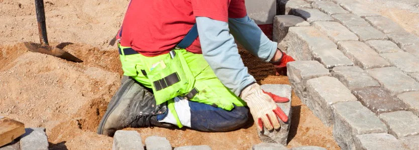 consttruction worker on their knees laying paver blocks
