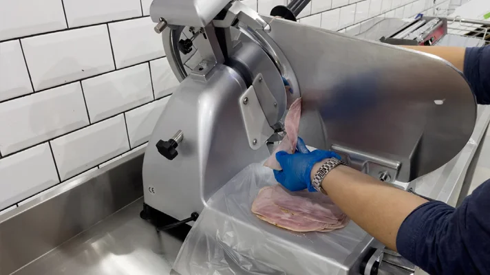 close up of person slicing ham on a commercial meat slicer