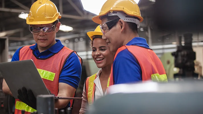 three individuals with hard hats and safety vests on looking at a clipboard