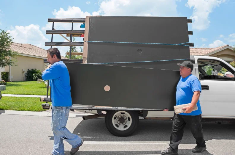 two construction workers carrying a sheet of countertop material